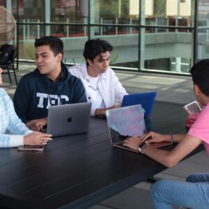 Group of young adults working and collaborating on laptops at an outdoor table.