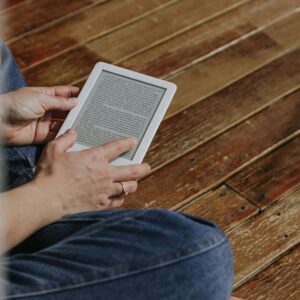 Close-up of hands holding an e-reader on a wooden floor, depicting a casual reading moment.