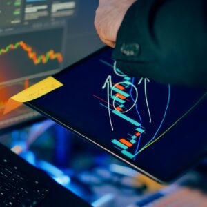 A business professional examines financial charts on a tablet and monitor for investment strategy.